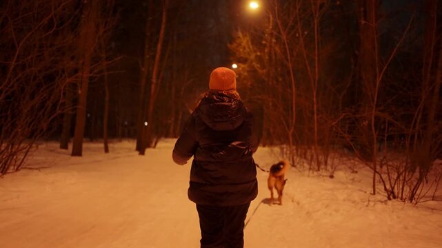 Woman walking her dog on a snowy street of a suburban area at night