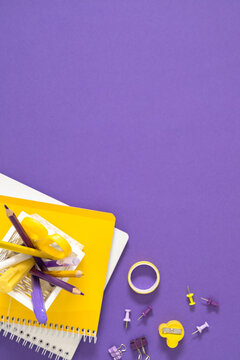 Vertical Yellow and Purple Stationery Flat Lay Corner Composition with Copy Space. Office School Supplies, Pencils, Scissors in Holder on Violet Background Top View. Minimalist Workspace Concept.