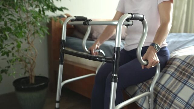 A young woman after a stroke gets out of bed using a walker. Close-up.