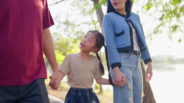 Asian young child holding hands mother and father in outdoors park. 