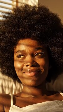 Young Black Woman Wakes Up in Sunlight - A close-up shot shows a young Black woman with an afro hairstyle opening her brown eyes. Warm sunlight rays cast shadows across her face as she looks upwards.