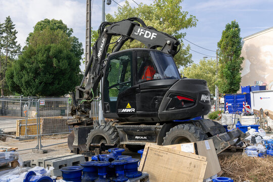 Nancy, France - August 1st 2026 : View of a 15-tonne black compact wheeled excavator Mecalac 15MWR on a construction site for work on the drinking water network.