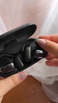 Woman placing wireless earbud into charging case after use, true wireless earphones, portable audio and battery charging concept.