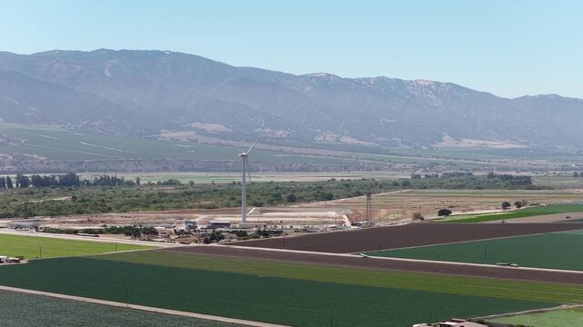 Lone wind turbine generating renewable energy among the vast agricultural fields of Salinas Valley in California, with the Gabilan Mountains providing a scenic backdrop on a clear day
