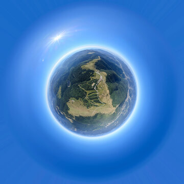 Aerial view of Le Markstein Station in the Vosges mountains featuring green slopes, winding roads, and surrounding forests in a tiny planet perspective in Fellering, Grand Est, France.
