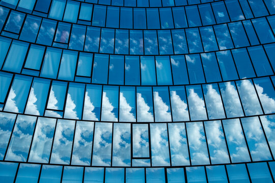 Passing clouds sweep through a curved surface of blue glass, while the facade lets windows extend sky reflection across the building and emphasize its architecture.