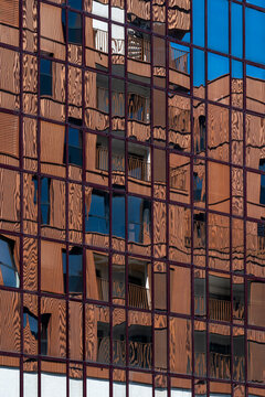 A restrained warm tone spreads as copper reflection over glass, while the facade sets a grid of windows around the neighboring building and its urban architecture.
