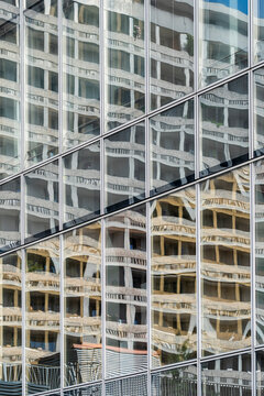 Fine diagonal seams cross a glass facade as layered imagery gathers in depth, while reflections fill the windows and merge nearby buildings into an urban grid of architecture.