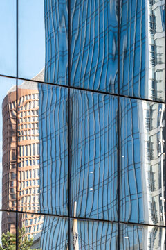 Within the frame, a tower bends inside a blue reflection on glass, while the facade and vertical windows stretch the building until architecture becomes controlled distortion.
