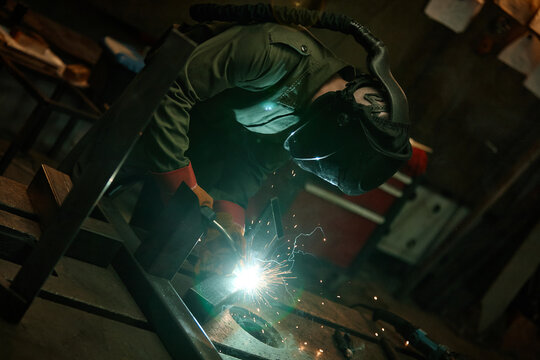 Young adult Caucasian male welder in protective mask welding metal in workshop, creating bright sparks. Image suitable for industrial manufacturing and vocational training promotions