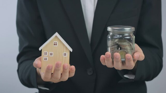 Proud person holding wooden home and glass coin jar, showing successful finance saving goal toward stable future family ownership