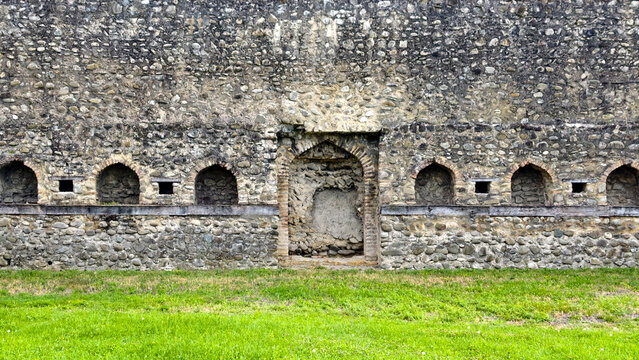 Ancient stone wall with a central arched entrance and symmetrical alcoves, showcasing historical architecture, texture, and the passing of time