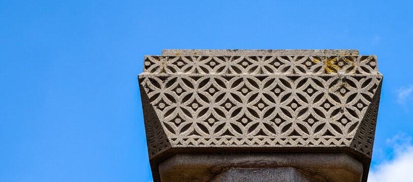 Stone monument detail featuring intricate geometric carving patterns. Showcasing ancient architectural design elements against a clear blue sky