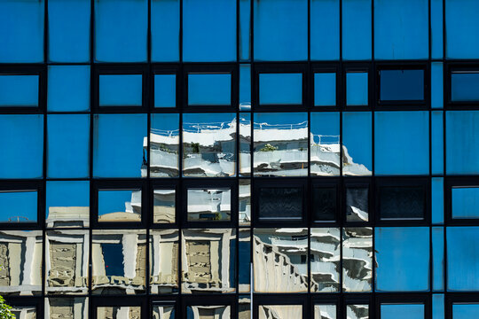 Ornate detail from a historic building appears in reflection across the frame, while blue glass over the facade lets windows create contrast within urban architecture.