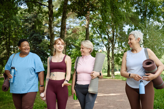 Diverse multiethnic group of women walking in park after yoga class, carrying mats and talking. Image represents active lifestyle and wellness, suitable for healthcare marketing