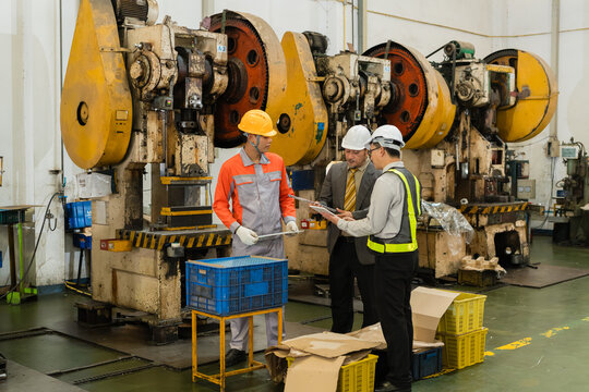 Manager and engineer reviewing production checklist with machine operator beside power presses ensuring precision and quality in a modern industrial manufacturing environment with heavy machinery