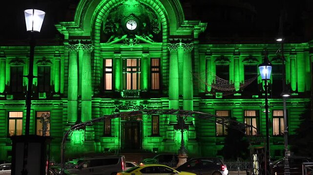Historical building facade illuminated with bright green light at night in Bucharest.