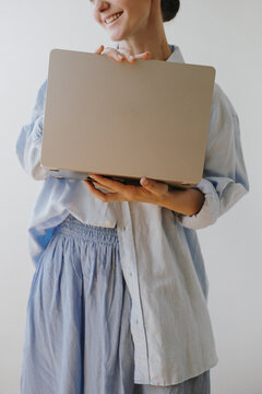 Female Model Standing In Light Blue Outfit Holding Silver Laptop Facing Camera Against Plain Wall