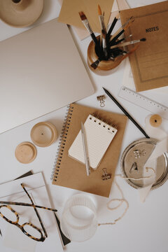 Cozy Creative Desk Setup With Craft Notebooks, Paintbrushes, Candle, And Pearl Accessories