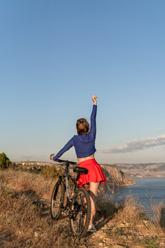 Bicycle cyclist mountains, woman standing with mountain bike on cliff edge overlooking sea during sunset with copy space for text