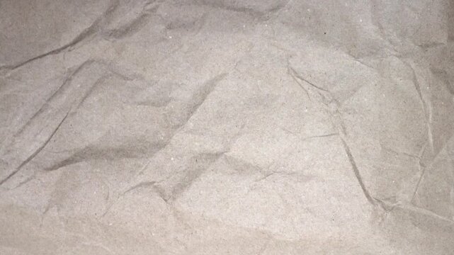 Paper texture background video, close-up of crumpled kraft paper with soft blur lighting. Vintage paper texture with crease, stain, grain, dust particles, 4K stop motion video