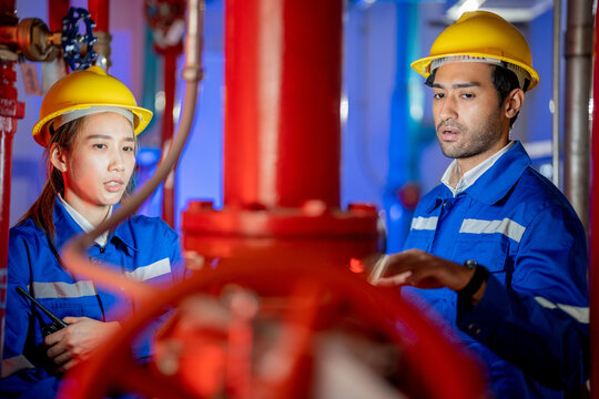 A female and a male engineer discussing beside the red fire pump piping in a fire pump room with red piping and valves. Ideal for industrial and construction media.