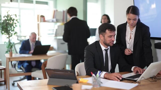 Woman head of a bank office stands with a male employee and helps with work issues and filling out documents on a laptop. Office employees working on a laptop . High quality 4k footage