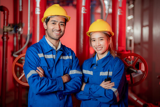 A female and a male engineer posing together with a warm team smile in a fire pump room with red piping and valves. Modern mechanical and electrical engineering.