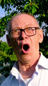 An elderly man performs an overacted expression of surprise with exaggerated facial movements, making the footage suitable for humor, comedy, advertising, reactions and entertainment. Close up.