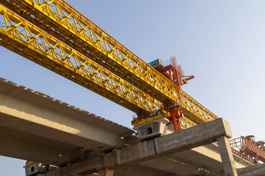 Mega infrastructure development showing segmental bridge assembly in daylightConcrete highway support columns and yellow truss bridge launcher machinery