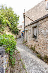 Fototapeta premium Picturesque Croatian Mediterranean island village featuring traditional stone houses with weathered facades, narrow cobblestone alley, and rustic architecture.
