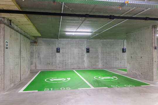 Electric cars parking lot. Modern underground concrete parking garage featuring bright green spaces marked with white electric vehicle charging symbols and wall-mounted EV chargers.