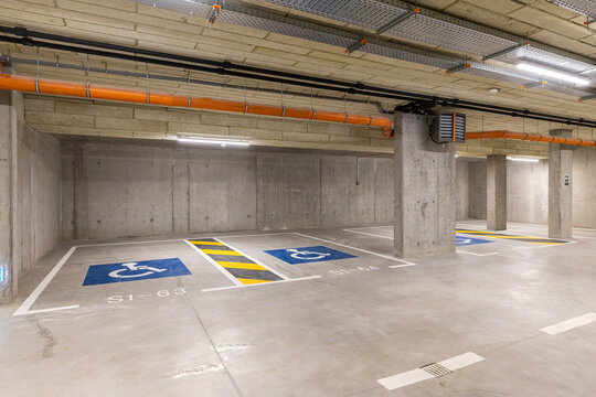 Modern underground concrete parking garage featuring designated handicap accessible spaces marked with blue wheelchair symbols and safety floor lines under bright ceiling lights