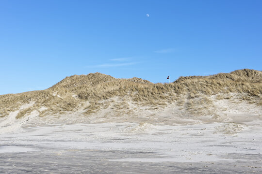 D&uuml;nenlandschaft an der Nordsee in D&auml;nemark bei Tornby mit d&auml;nischer Flagge in den D&uuml;nen und Mond am Tage