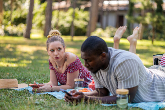 Couple experiencing phubbing during outdoor picnic in park