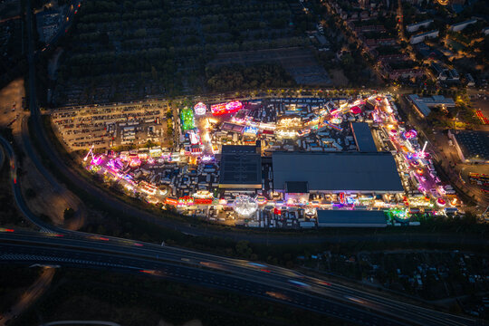 Aerial view of Parc Expo Mulhouse illuminated at night with vibrant fairground rides, colorful lights, and surrounding parking areas in Mulhouse, Grand Est, France.