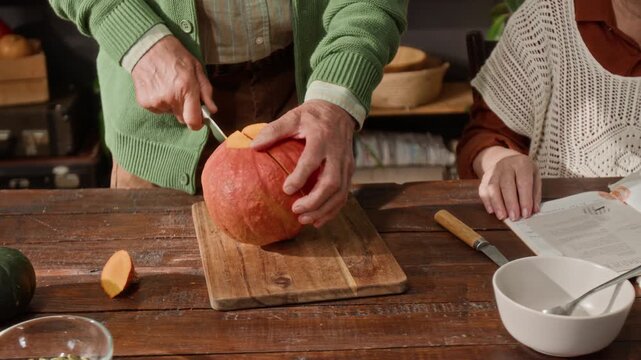 Senior man cutting fresh pumpkin on wooden board while senior woman watches. High angle shot ideal for senior lifestyle, healthy cooking, and retirement living commercials