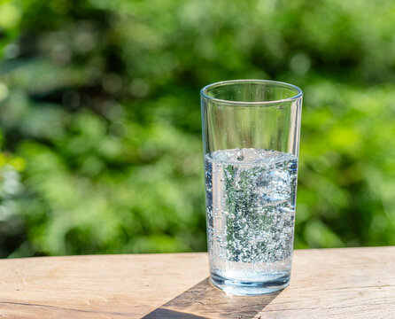 Clear glass of sparkling mineral water with bubbles on wooden table outdoors.