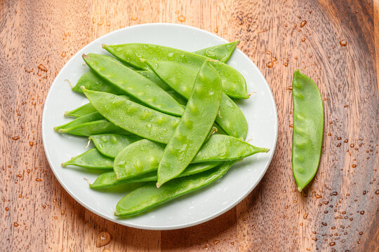 Top view of a heap of fresh green snow peas served on a white ceramic plate