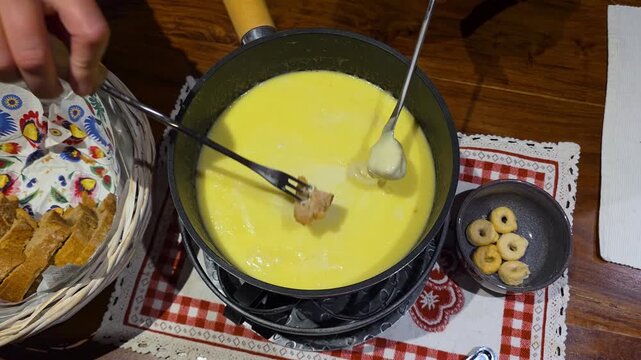 Close up of hands dipping bread into a bubbling pot of authentic Swiss cheese fondue. Perfect for culinary, hospitality, and home dining content.