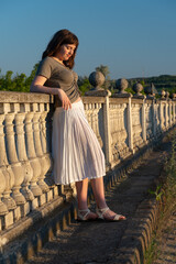 Obraz premium Young woman in white skirt leaning on stone balustrade at sunset