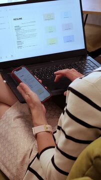 Woman using her smartphone and laptop to refine her resume with an AI assistant, fixing grammar errors and optimizing the content for a standout CV