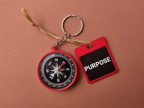 A red keychain compass attached with a string to a red tag labeled PURPOSE on a brown surface