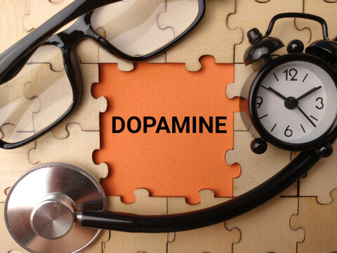 A stethoscope, alarm clock, glasses, and wooden puzzle pieces framing a orange center printed with DOPAMINE