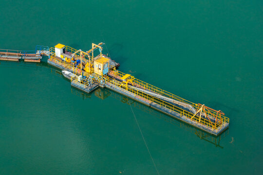Aerial view of a floating sand mining platform on green water with yellow metal structures and a small boat in Poland.