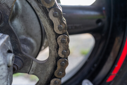 Worn motorcycle chain wrapped around rusty rear sprocket close up