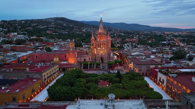 A cinematic aerial drone view capturing the distinctive pink stone spires of the Parroquia de San Miguel Arc&aacute;ngel glowing at dusk.
