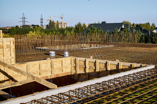 High-angle wide horizontal view of a building construction site showing a large tied rebar reinforcement grid, vertical starter bars, and wooden OSB formwork, prepared for pouring a concrete floor sla