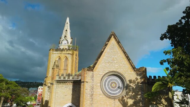 Historic gothic Trinity Cathedral tower and rose window stand against dramatic storm clouds and blue sky in Port of Spain Trinidad