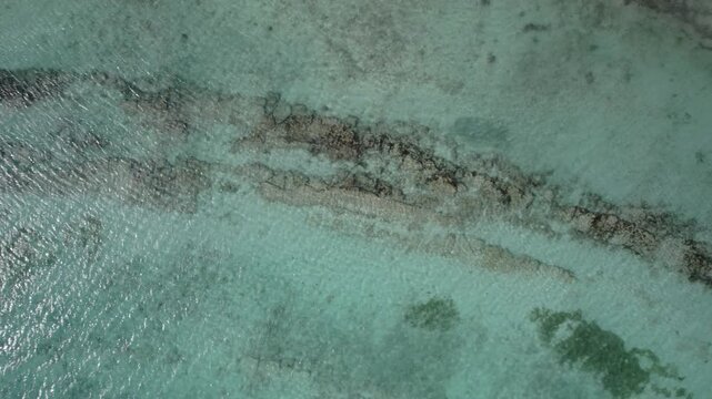 Drone shot reveals shallow coral reef patterns in clear turquoise water, tropical coast